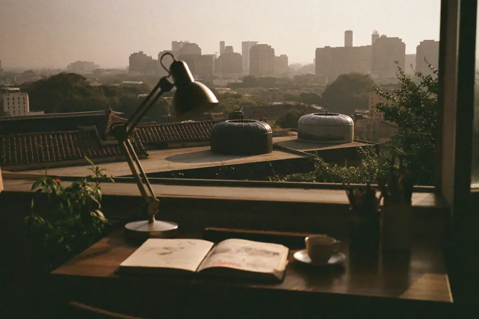 A studio desk by an open window overlooking Delhi rooftops at golden hour