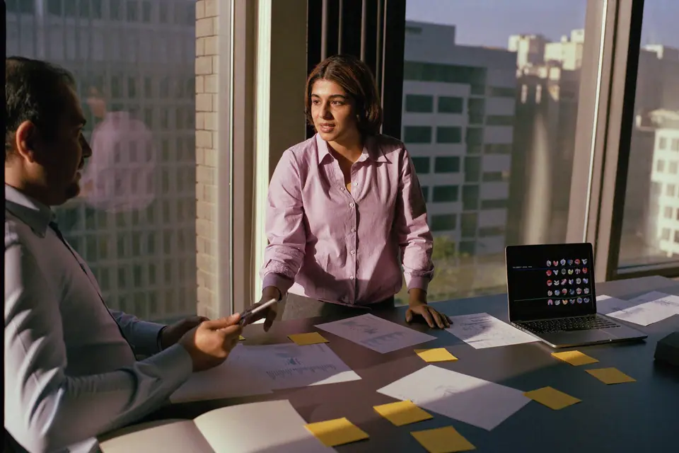 Two colleagues planning a workflow over printed charts and sticky notes